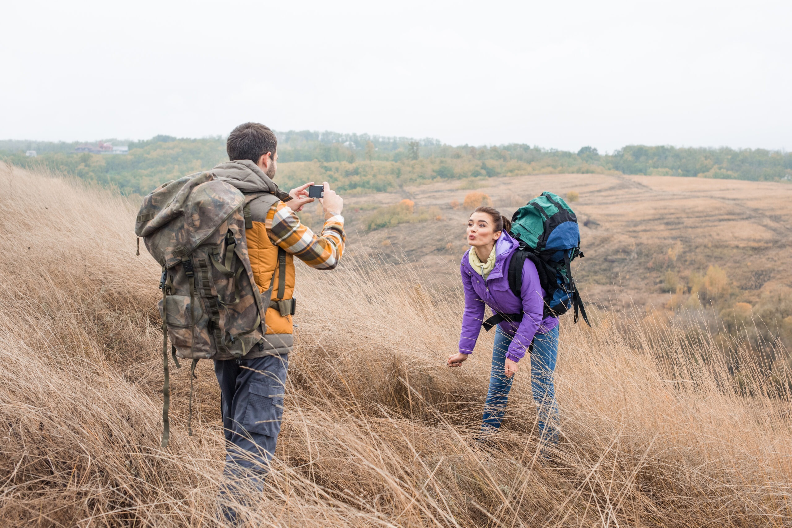 Young man photographing beautiful brunette woman during walking tour in countryside