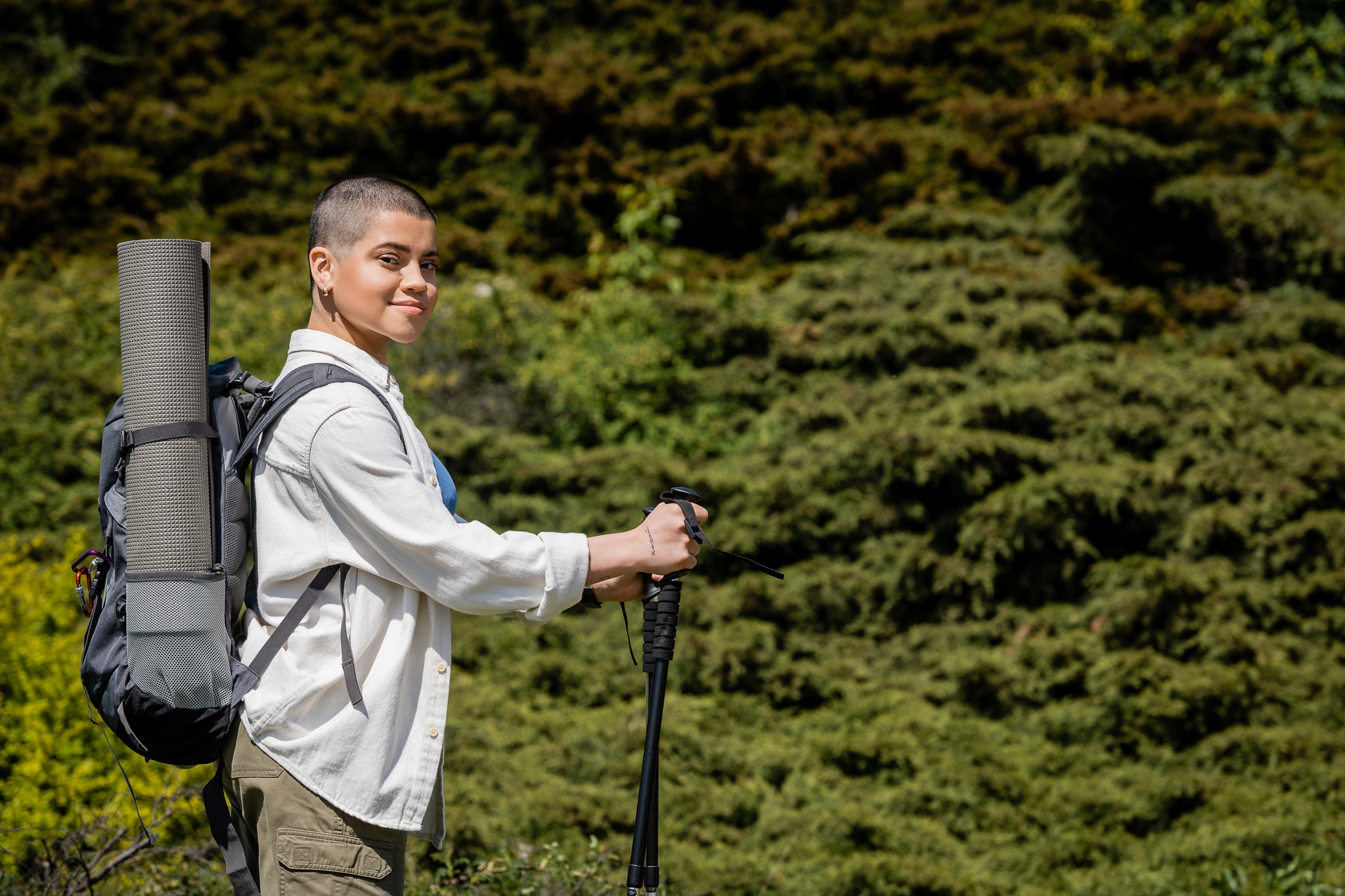 Smiling young short haired female hiker with backpack holding tr